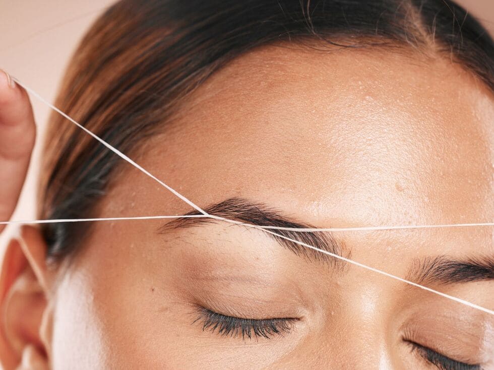 Rostro de cerca recibiendo una depilacion de cejas con hilo