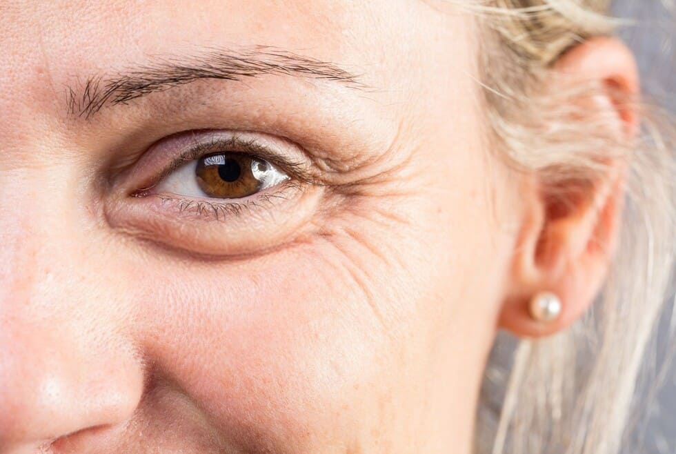 Detalle de la piel madura mostrando la textura de las arrugas finas y líneas de expresión en la zona ocular.